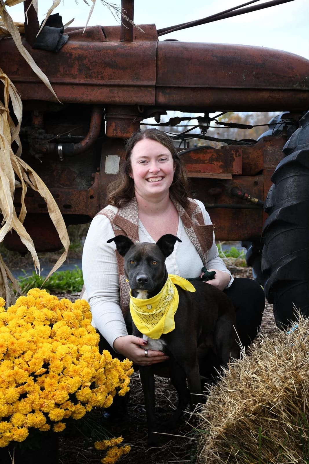 Portrait of Brittany Aylott, board member, kneeling with a black rescue dog in a yellow bandana